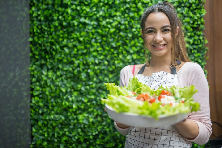 Woman in apron presenting a fresh vegetable salad. Perfect for healthy living and cooking themes.