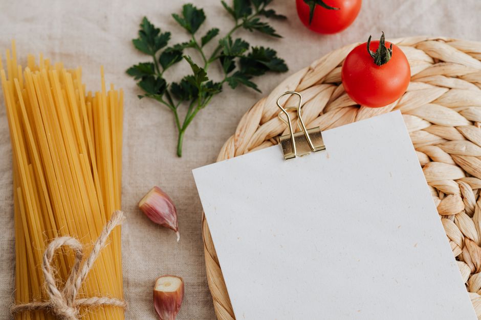 Flat lay of pasta, garlic, and tomatoes on a woven mat, perfect for Italian cooking inspiration.